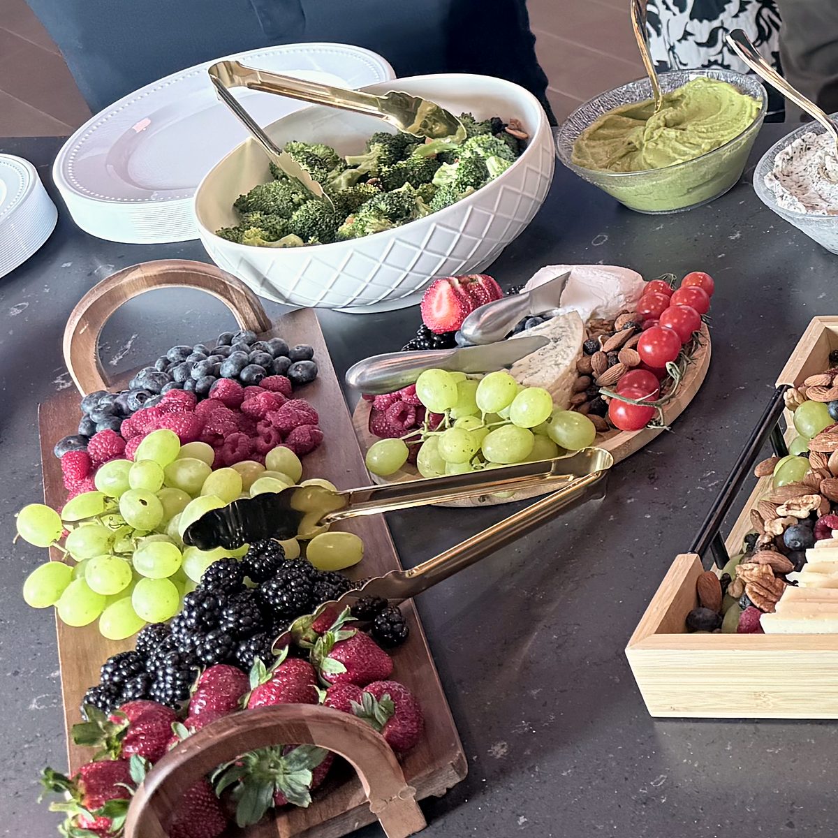 Wooden fruit board with grapes, blueberries, raspberries, blackberries and strawberries next to broccoli salad, dips and a cheese tray at a corporate event