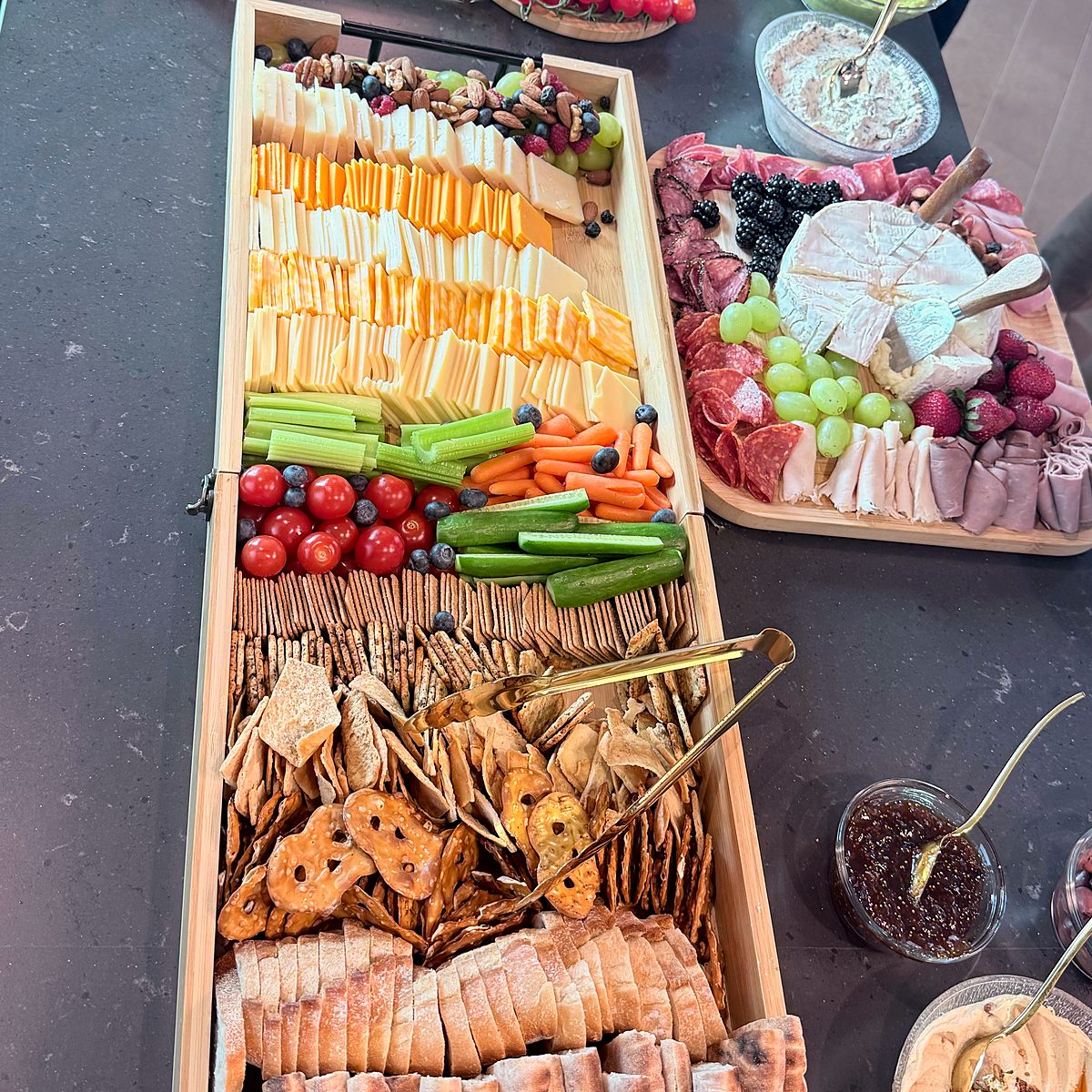 Overhead view of a Thyme Catering grazing tray of cheeses, fresh vegetables, crackers, pretzel crisps and sliced bread beside a charcuterie board with brie